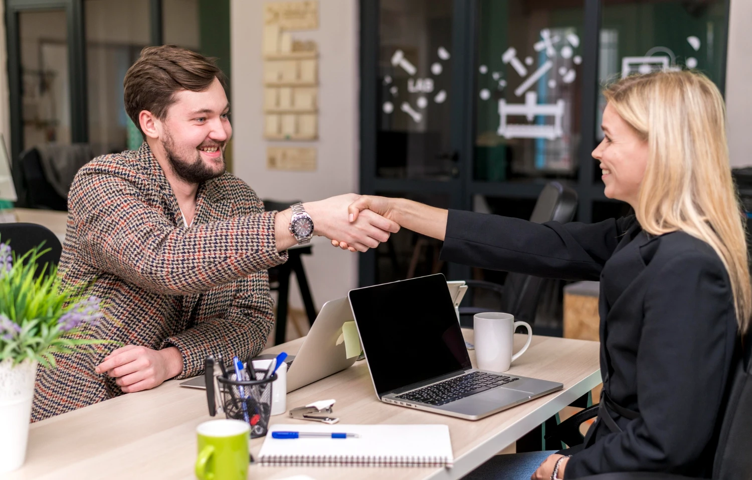 Man and woman shaking hands across a desk in a professional office setting.